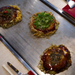 三國志　〒721-0907 広島県福山市春日町６丁目９−１０ oko_sangoku 広島名物お好み焼き、鉄板焼き 広島名物 広島風お好み焼き、多くの種類のトッピングの組み合わせで、 オリジナルお好み焼きをお楽しみ下さい。広島県 福山市 福山東インターチェンジから 車で約１０分 広島 お好み焼の お店。キャベツたっぷり　生麺使用　数種のスパイスが隠し味　鉄板で熱々のお好み焼を是非！　冷凍お好み焼販売中　ご家庭にストック　いつでも美味しい。「お好み焼・鉄板焼　三國志」（福山市春日町6-9-10、藤井啓文代表）はこのほど、冷凍お好み焼きを開発して販売を始めた。 　コロナ禍で店内での飲食が減る中、スーパーやコンビニでは冷凍食品の需要が増えていることから、お好み焼きの冷凍販売を思いついたという。「二四時間、出来たての味を楽しんでほしい」と昨年から開発に乗り出した。「レンジで温めた際、店内で食べるお好み焼きと同じ状態になるよう工夫した」と藤井代表。店内で提供する物と同じ材料で焼き上げ、専用の機械で急速冷凍する。レンジでの加熱を考慮し、焼く時間を通常の七─八割に抑えて調整を重ねたという。 　肉玉（760円）、イカ・エビ・肉玉入りの「三國志スペシャル」（1040円）をはじめ、イカ天肉玉（880円）、チーズ肉玉（860円）など約10種類がある。 　レンジで温める時間は七分前後。肉玉の場合は裏返して三分、表にして四分温める。最後に別袋入りのソースをかければ完成。同店ならではの、飽きのこないやさしい味が楽しめる。常連客からは「店で食べるのと同じくらいおいしかった 「冷凍庫にストックしておいて、食べたい時に食べられるのがうれしい」といった声が寄せられているとか。藤井代表は「自宅用やお土産にぜひどうぞ。準備が整えば、地方発送も始めます」と話す。 　なお、夏をめどに価格の改定を行う予定。また一度に10枚以上購入する場合は、一週間前までに予約が必要。 　ホルモン焼き（860円）や焼きそば（710円）など鉄板焼きメニューの冷凍商品も用意している。