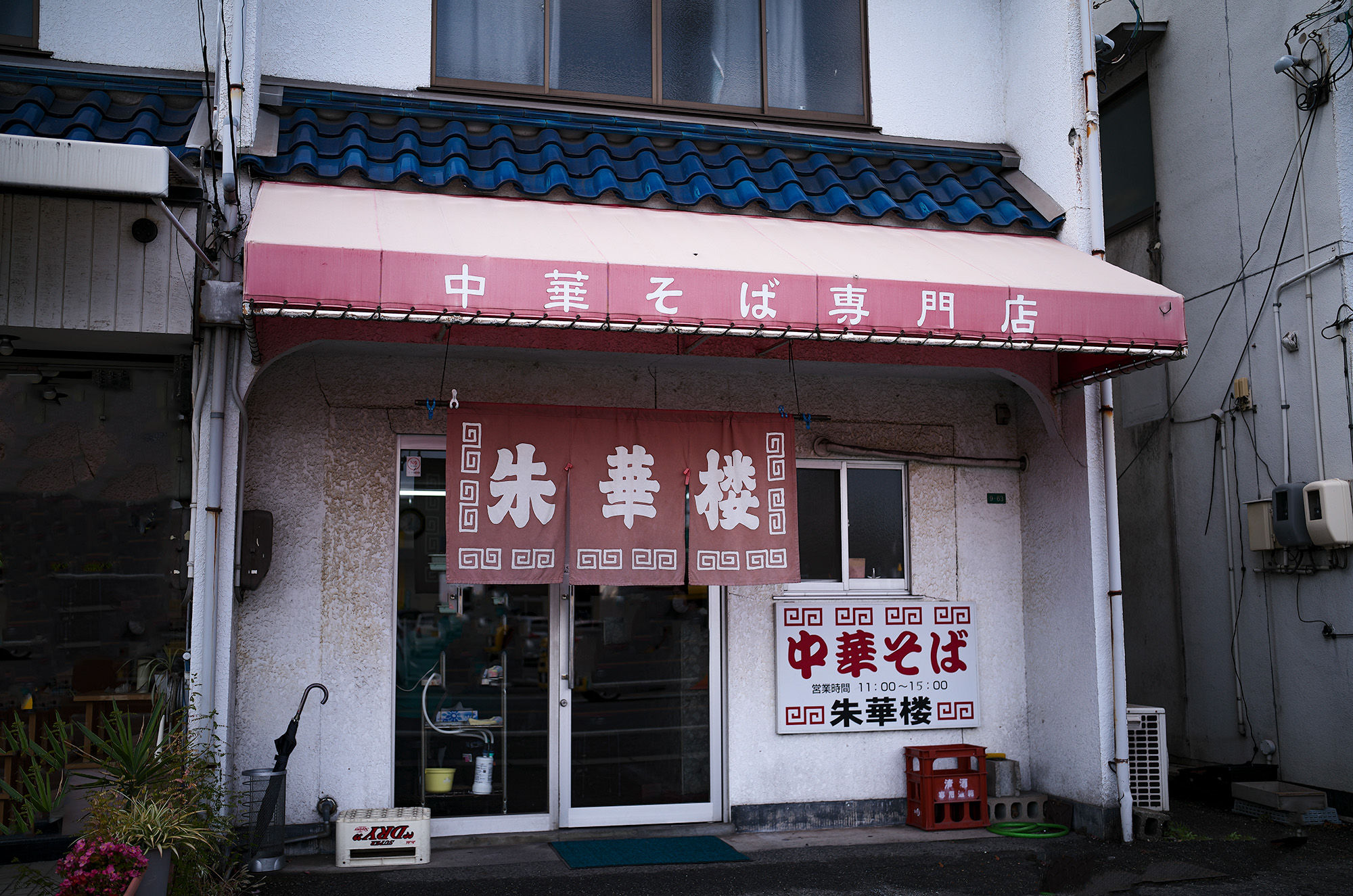 朱華楼 ・東深津店　〒721-0974 広島県福山市東深津町１丁目９−６３　しゅうかろう　ラーメン らーめん いなり　愛知 名古屋 Alto e Diritto altoediritto アルトエデリット 国道２号線と１８２号線の交わる交差点の西に福山通運のある交差点を北上。高架を通り抜け２００メートル程北上した左側（ゴルフショップダイナマイト駐車場の道路を挟んで向かい側）東福山駅から1,362m　中華そば 専門店 広島県 ひろしま 尾道ラーメン 尾道ラーメン。広島県東部の尾道市から福山市で広がるご当地ラーメン。鶏ガラ中心の醤油スープに、大粒の背脂が浮かぶのが特徴。瀬戸内産のいりこを使っているお店も多い。名前は全国的に知られているが、実は現地には20～30軒しかない珍しいご当地ラーメンだ。一番の有名店は尾道市の「朱華園」。1947年に屋台から始まったお店で、全国からお客の集まる行列店だったが、2019年6月に惜しまれつつも閉店。ラーメン業界的には大きなニュースになった。「朱華園」は閉店してしまったものの、そのDNAを受け継ぐお店がいくつかある。今回ご紹介するのは、そんな「朱華園」の流れを汲む「朱華楼」。福山市内で3店舗を展開しているが、東深津店が代表として語られることが多い。メニューは「中華そば」と「いなり寿司」のみ。中華そばは600円だ。