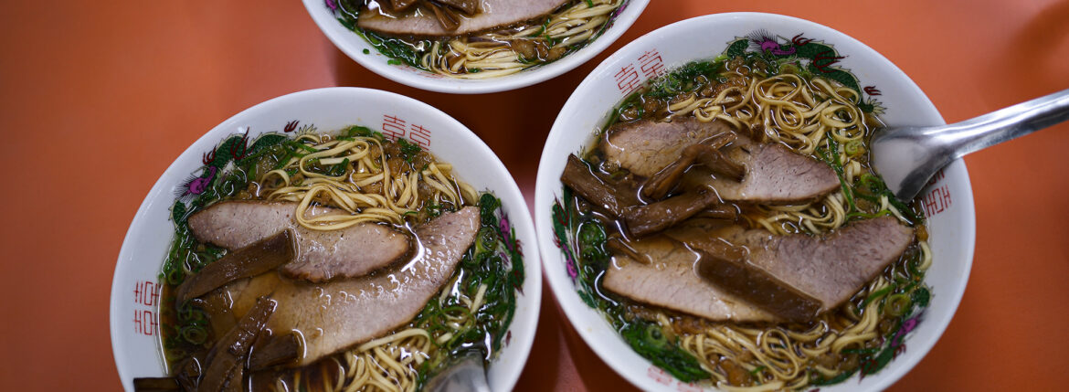 朱華楼 ・東深津店　〒721-0974 広島県福山市東深津町１丁目９−６３　しゅうかろう　ラーメン らーめん いなり　愛知 名古屋 Alto e Diritto altoediritto アルトエデリット 国道２号線と１８２号線の交わる交差点の西に福山通運のある交差点を北上。高架を通り抜け２００メートル程北上した左側（ゴルフショップダイナマイト駐車場の道路を挟んで向かい側）東福山駅から1,362m　中華そば 専門店 広島県 ひろしま 尾道ラーメン 尾道ラーメン。広島県東部の尾道市から福山市で広がるご当地ラーメン。鶏ガラ中心の醤油スープに、大粒の背脂が浮かぶのが特徴。瀬戸内産のいりこを使っているお店も多い。名前は全国的に知られているが、実は現地には20～30軒しかない珍しいご当地ラーメンだ。一番の有名店は尾道市の「朱華園」。1947年に屋台から始まったお店で、全国からお客の集まる行列店だったが、2019年6月に惜しまれつつも閉店。ラーメン業界的には大きなニュースになった。「朱華園」は閉店してしまったものの、そのDNAを受け継ぐお店がいくつかある。今回ご紹介するのは、そんな「朱華園」の流れを汲む「朱華楼」。福山市内で3店舗を展開しているが、東深津店が代表として語られることが多い。メニューは「中華そば」と「いなり寿司」のみ。中華そばは600円だ。