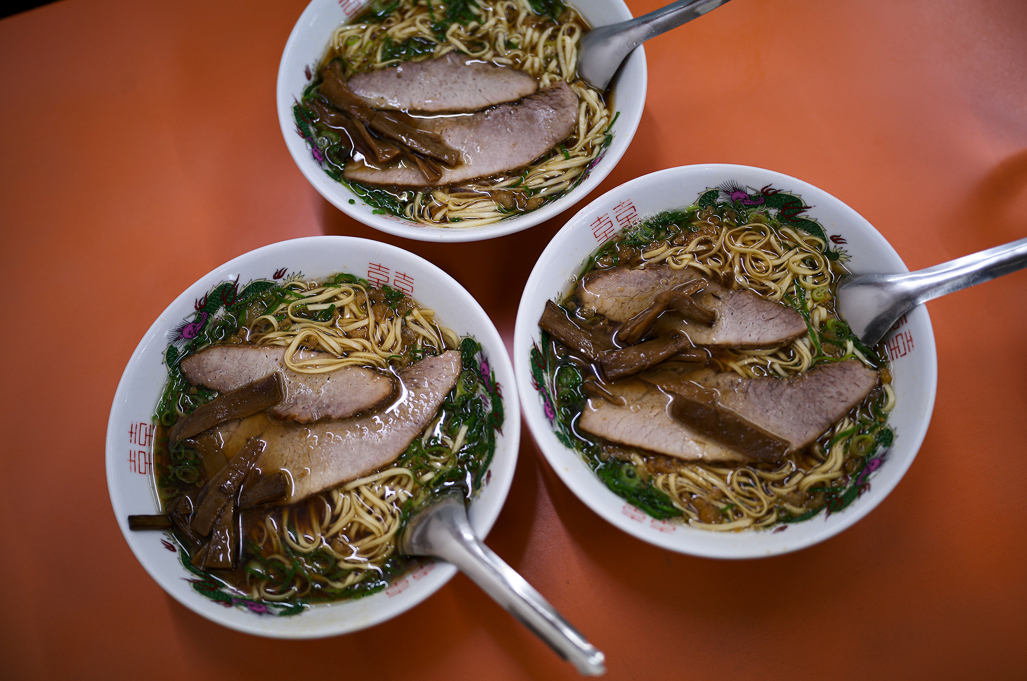 朱華楼 ・東深津店　〒721-0974 広島県福山市東深津町１丁目９−６３　しゅうかろう　ラーメン らーめん いなり　愛知 名古屋 Alto e Diritto altoediritto アルトエデリット 国道２号線と１８２号線の交わる交差点の西に福山通運のある交差点を北上。高架を通り抜け２００メートル程北上した左側（ゴルフショップダイナマイト駐車場の道路を挟んで向かい側）東福山駅から1,362m　中華そば 専門店 広島県 ひろしま 尾道ラーメン 尾道ラーメン。広島県東部の尾道市から福山市で広がるご当地ラーメン。鶏ガラ中心の醤油スープに、大粒の背脂が浮かぶのが特徴。瀬戸内産のいりこを使っているお店も多い。名前は全国的に知られているが、実は現地には20～30軒しかない珍しいご当地ラーメンだ。一番の有名店は尾道市の「朱華園」。1947年に屋台から始まったお店で、全国からお客の集まる行列店だったが、2019年6月に惜しまれつつも閉店。ラーメン業界的には大きなニュースになった。「朱華園」は閉店してしまったものの、そのDNAを受け継ぐお店がいくつかある。今回ご紹介するのは、そんな「朱華園」の流れを汲む「朱華楼」。福山市内で3店舗を展開しているが、東深津店が代表として語られることが多い。メニューは「中華そば」と「いなり寿司」のみ。中華そばは600円だ。